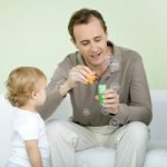 Father and toddler blowing bubbles together