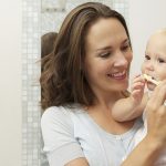 Mother teaching baby how to brush teeth with toothbrush