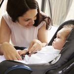 Mother Putting Baby Son Into Car Travel Seat