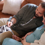 Expectant Couple looking ultrasound images of baby in living room