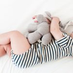 Baby wearing striped onesie sleeping with a stuffed animal