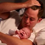 Father Lying In Bed With Crying Baby Daughter