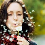 Girl blowing on white dandelion in the forest