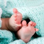 Two cute tiny baby feet wrapped in a blue-green aqua knitted blanket.