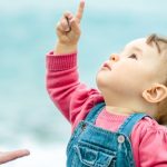 baby-in-denim-sits-on-the-beach-and-looks-up-picture-id1145518928