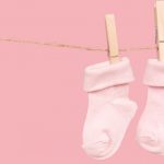 pair-of-pink-baby-socks-on-a-clothesline-on-a-pink-background-with-picture-id860524336