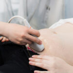 Close-up Of Doctor Moving Ultrasound Probe On Pregnant Woman’s Stomach In Hospital