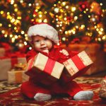 Happy baby by Christmas tree with gifts
