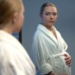 Pregnant woman looking in mirror reflection, expecting baby birth, young mother