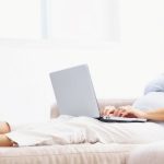Middle aged pregnant lady working on laptop while lying on the sofa at home