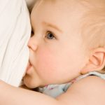The small blue-eyed girl sucks a breast close up