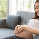 attractive-pregnant-woman-is-sitting-in-sofa-and-holding-her-belly-picture-id1095013806