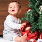 cute child with christmas tree.  happy baby sitting near a fir tree and holding a christmas ornament