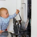 Toddler child, boy, helping mom, putting dirty dishes in dishwasher at home,