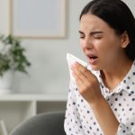 Suffering from allergy. Young woman with tissue sneezing at home, space for text