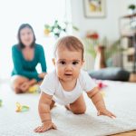Mother and baby girl at home, baby crawling and looking for toys