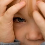 Boy peeking from behind his hands.