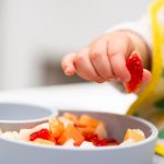 macro-close-up-of-baby-hand-with-a-piece-of-fruits-sitting-in-childs-picture-id1209984842 (1)