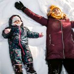 Mother and baby girl making an angel in snow. High angle view