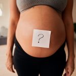 Torso of Caucasian pregnant female standing upright with question mark on belly. Gender reveal, modern lifestyle