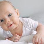 Closeup portrait of adorable infant baby boy lying on white blanket on stomach, smiling. Concept of children, baby, parenthood, childhood, life, maternity, motherhood