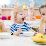 Funny little kid with open mouth eating in kindergarten group